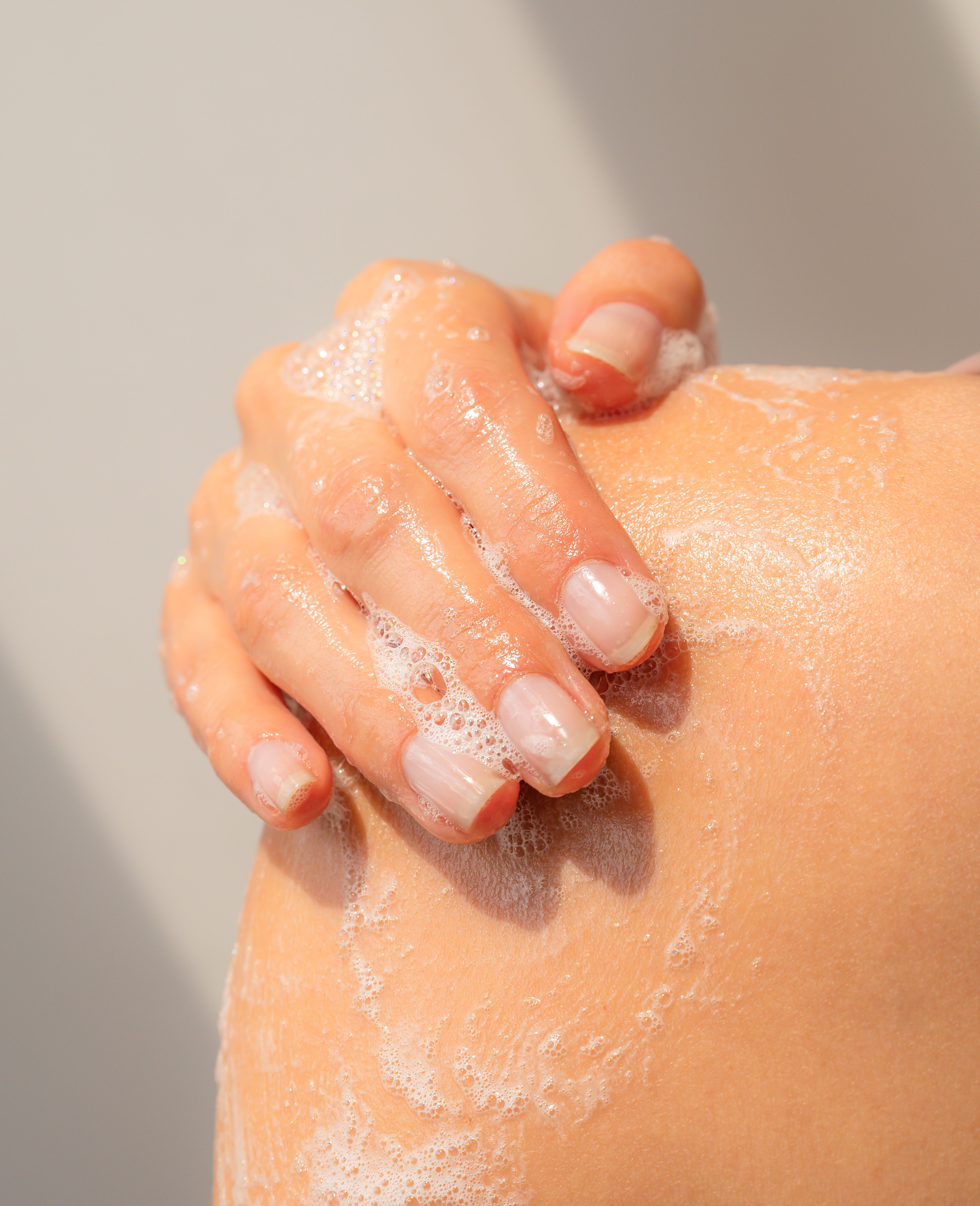 hand applying gentle body soap to skin in shower using a creamy lather